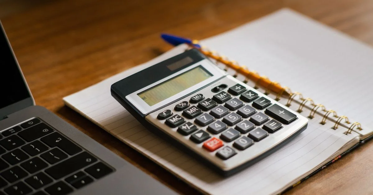 Calculatrice et ordinateur portable ouvert sur un bureau en bois, idéal pour des tâches financières ou comptables.