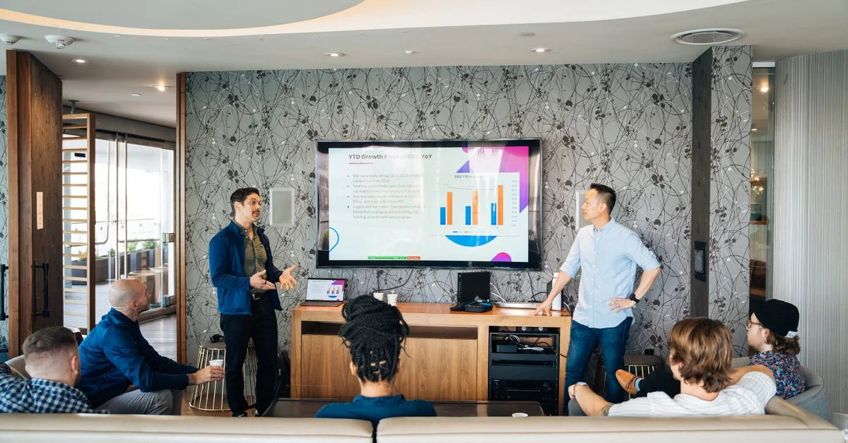 Groupe de professionnels participant à une présentation d'affaires avec une télévision affichant des graphiques.