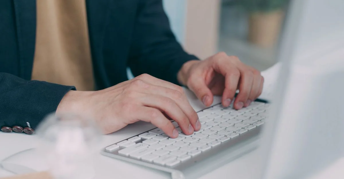 Gros plan sur des mains tapant sur un clavier blanc dans un environnement de bureau. Idéal pour des thèmes d'affaires ou de technologie.